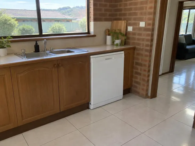 Kitchen sink and white dishwasher under a timber benchtop with brick wall and tiled floor in Swansea