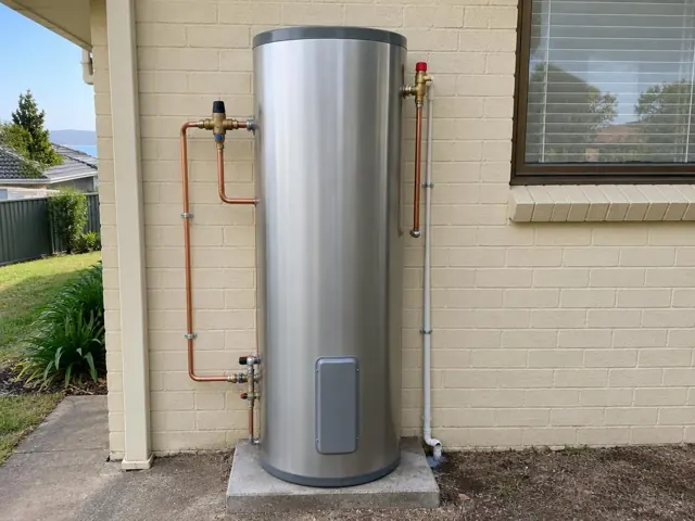 Newly installed cylindrical hot water system beside a brick house wall and window in Caves Beach