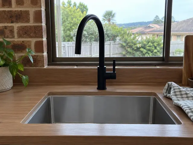 Black kitchen mixer tap over stainless sink with timber benchtop and brick wall in Pinny Beach